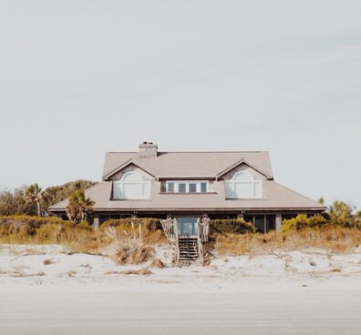 A house sitting on the beach in front of some sand dunes.